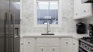 A modern kitchen with white cabinetry, a built-in stove, and a window with blinds.