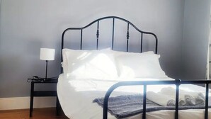A neatly made bed with white linens in a room with a grey wall and a black metal headboard.