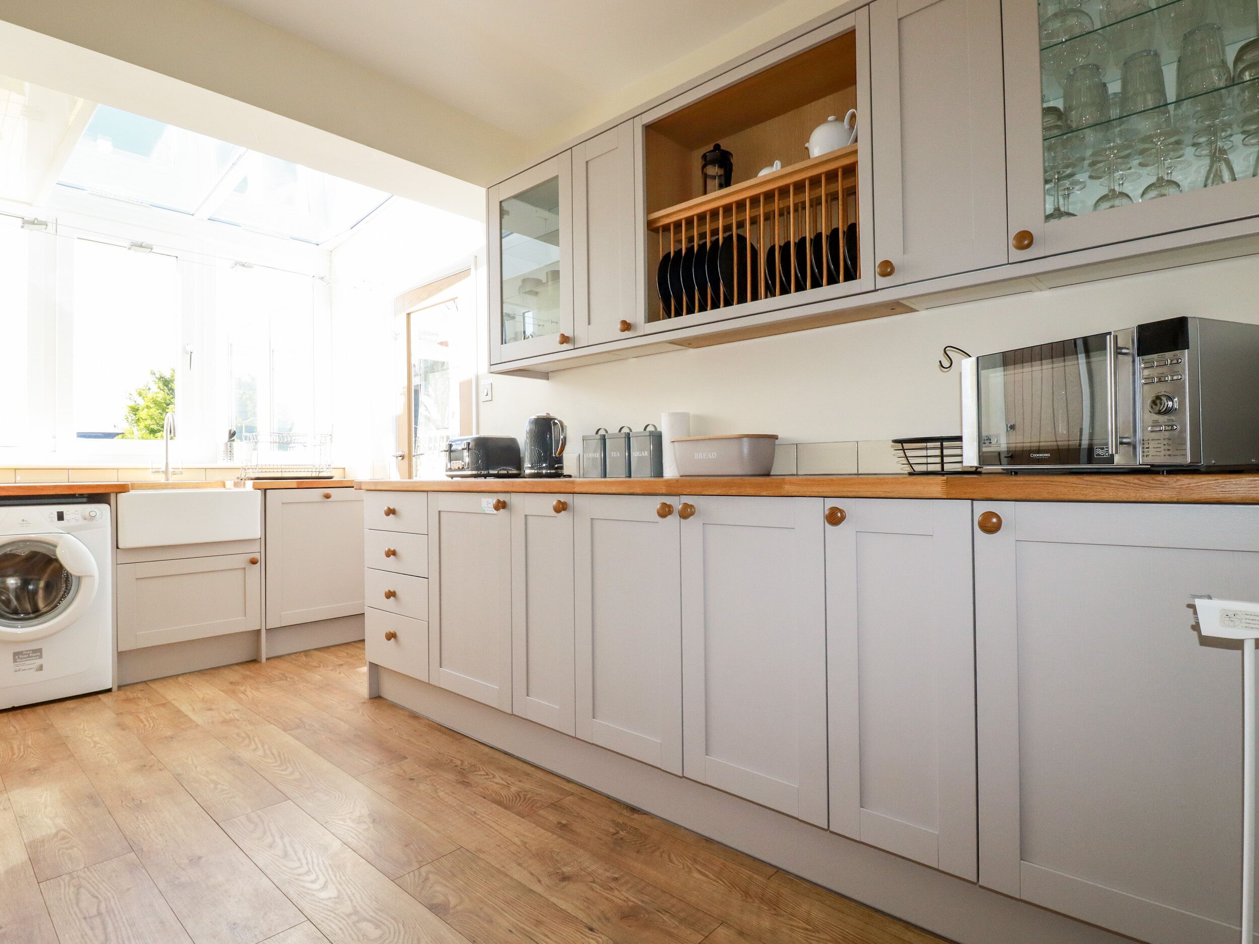 A modern kitchen with wooden countertops, white cabinets, a built-in washing machine, and a microwave.