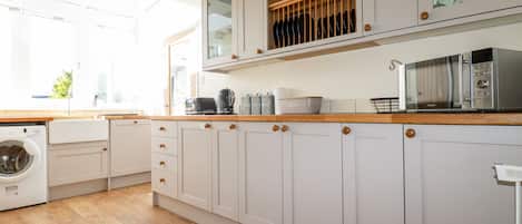 Een moderne keuken met houten aanrechtbladen, witte kastjes, een ingebouwde wasmachine en een magnetron.