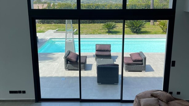 Una habitación moderna con amplios ventanales que dan a una piscina y una vista panorámica de colinas y palmeras.