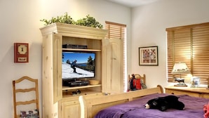 A bedroom with a bed, a wooden TV stand with a TV displaying a ski scene, a small table with a lamp, and a chair. - Boulder Bay Lakefront. Dock, hot tub, BBQ, fire pit, pool table. Large backyard. (Big Bear Lake)