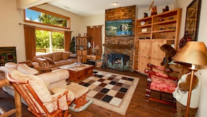 A cozy living room with a fireplace, wooden furniture, and a large window. - Boulder Bay Lakefront. Dock, hot tub, BBQ, fire pit, pool table. Large backyard. (Big Bear Lake)