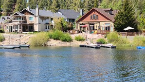 A lakeside cabin with a dock, surrounded by lush greenery and a forested backdrop. - Boulder Bay Lakefront. Dock, hot tub, BBQ, fire pit, pool table. Large backyard. (Big Bear Lake)