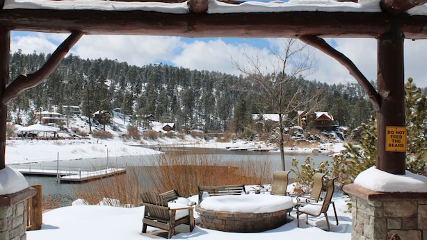 A wooden gazebo with snow-covered benches and a stone fireplace, overlooking a lake and a forested mountain. - Boulder Bay Lakefront. Dock, hot tub, BBQ, fire pit, pool table. Large backyard. (Big Bear Lake)
