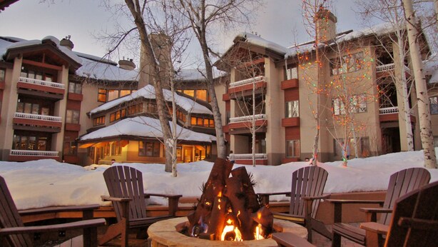 Un chalet doté de nombreux balcons, d’un foyer au centre et entouré d’un paysage enneigé.