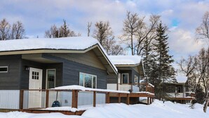 A cabin with a covered porch and a snow-covered roof, surrounded by trees.