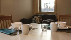 A dining table with white cups and a glass of water, set against a window with a view of buildings.