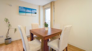 A dining area with a wooden table and four chairs, a potted plant, and a painting on the wall. - Bell Street Apartment (Glasgow)