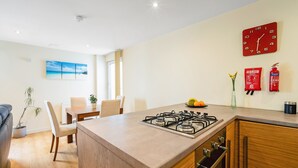 A modern kitchen with a gas stove, wooden cabinets, and a dining area with a table and chairs. - Bell Street Apartment (Glasgow)