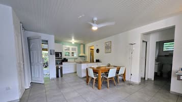 Une cuisine spacieuse avec un coin repas, des armoires blanches, un ventilateur de plafond et une vue sur l’extérieur.