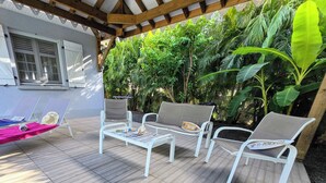 A patio with white metal furniture, including a table and two chairs, surrounded by lush greenery.