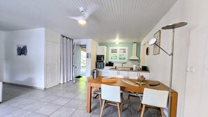 A modern kitchen with white cabinets, a dining area with a wooden table and chairs, and a ceiling fan.