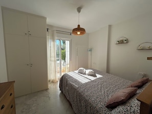 A bedroom with a bed, a wardrobe, a hanging light fixture, and a view of the outdoors.