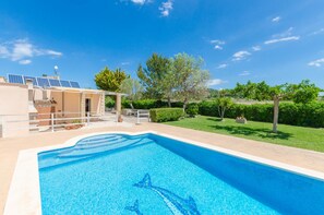 Uma piscina com design de golfinho, um edifício com painéis solares e um gramado bem cuidado.
