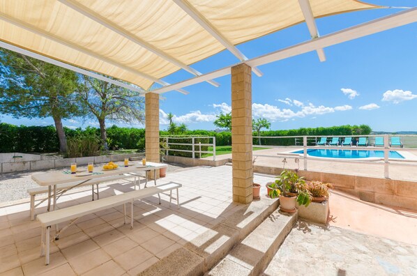 Un patio cubierto con piscina, mobiliario exterior y plantas en macetas.