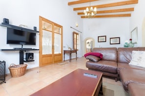 Una sala de estar con televisor, vigas de madera, candelabro, sofá y mueble para televisor.