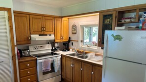 Una cocina con armarios de madera, estufa, refrigerador y ventana con vista a zonas verdes.