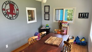 Comedor con mesa y sillas de madera, un reloj en la pared y una ventana con vistas a zonas verdes.