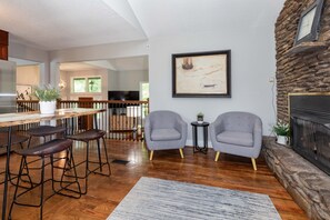 A modern living room with a stone fireplace, a dining area with wooden chairs, and a large painting on the wall.