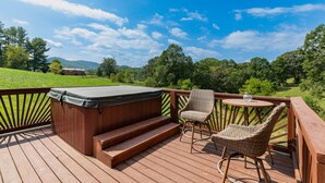 Una terraza de madera con un jacuzzi, sillas de mimbre y una mesa.
