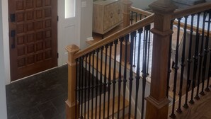 Un amplio salón con un gran ventanal, una escalera de madera y una araña.