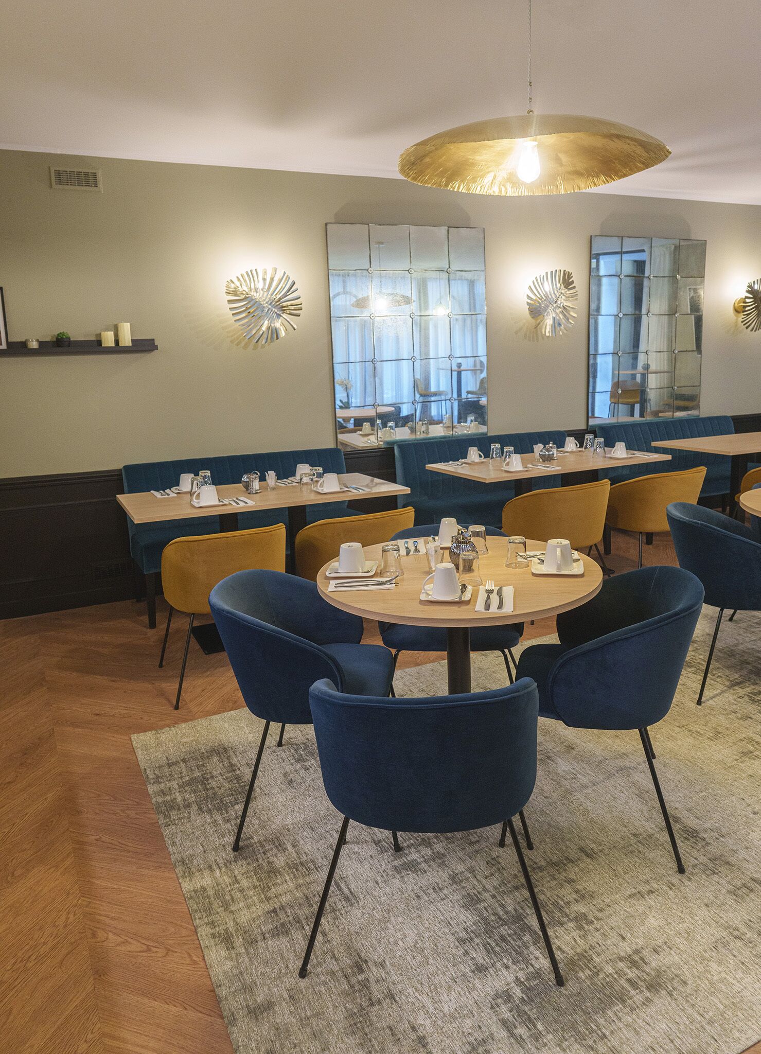 En restaurant med runde borde, blå og gule stole og en lysekrone i midten.