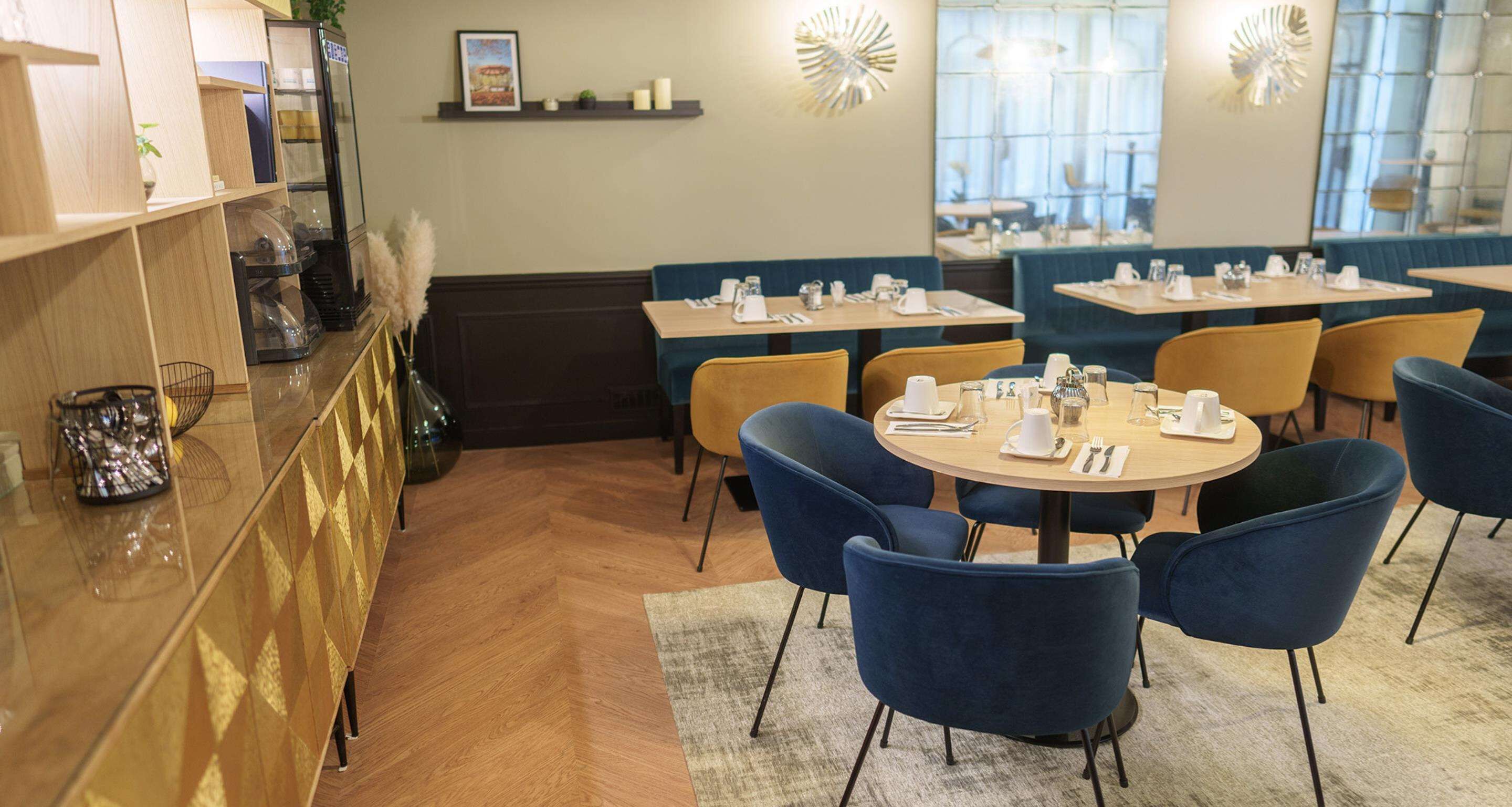 A restaurant with round tables, blue chairs, and a bar area with a glass display case.