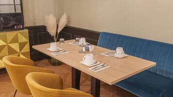 A dining area with a wooden table set for four, yellow chairs, a blue cushioned bench, and a decorative wall piece.