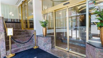 A hotel lobby with a marble reception desk, a black carpet with "LE PICARDY HOTEL" text, and a modern chandelier.