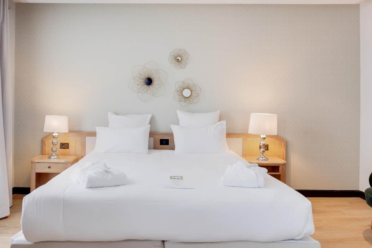 A large bed with white linens, two bedside tables with lamps, and decorative wall art.