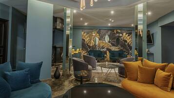 A modern living room with a round glass coffee table, blue and mustard sofas, and a unique ceiling light fixture.