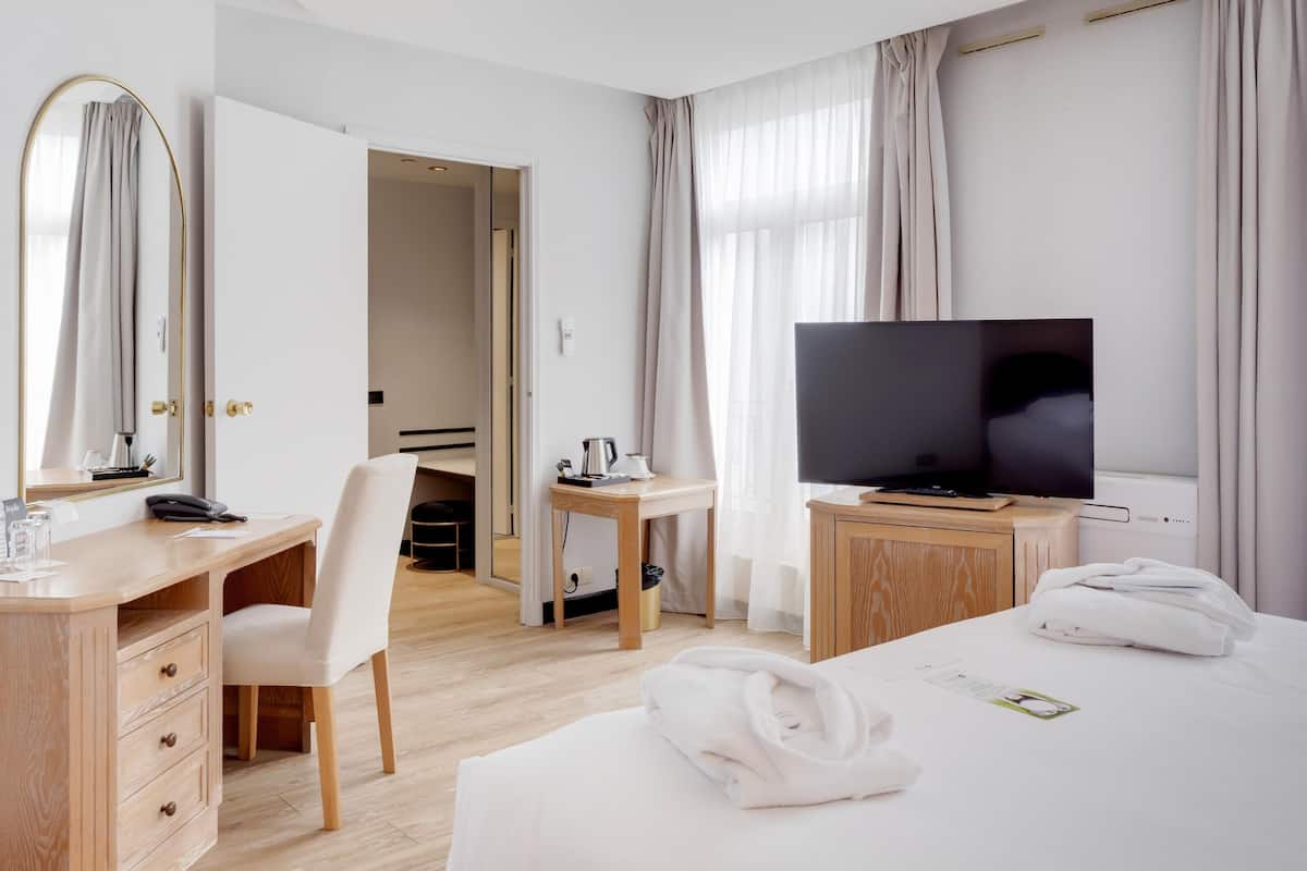 A hotel room with a desk, chair, TV, bed, and a bathroom visible through an open door.