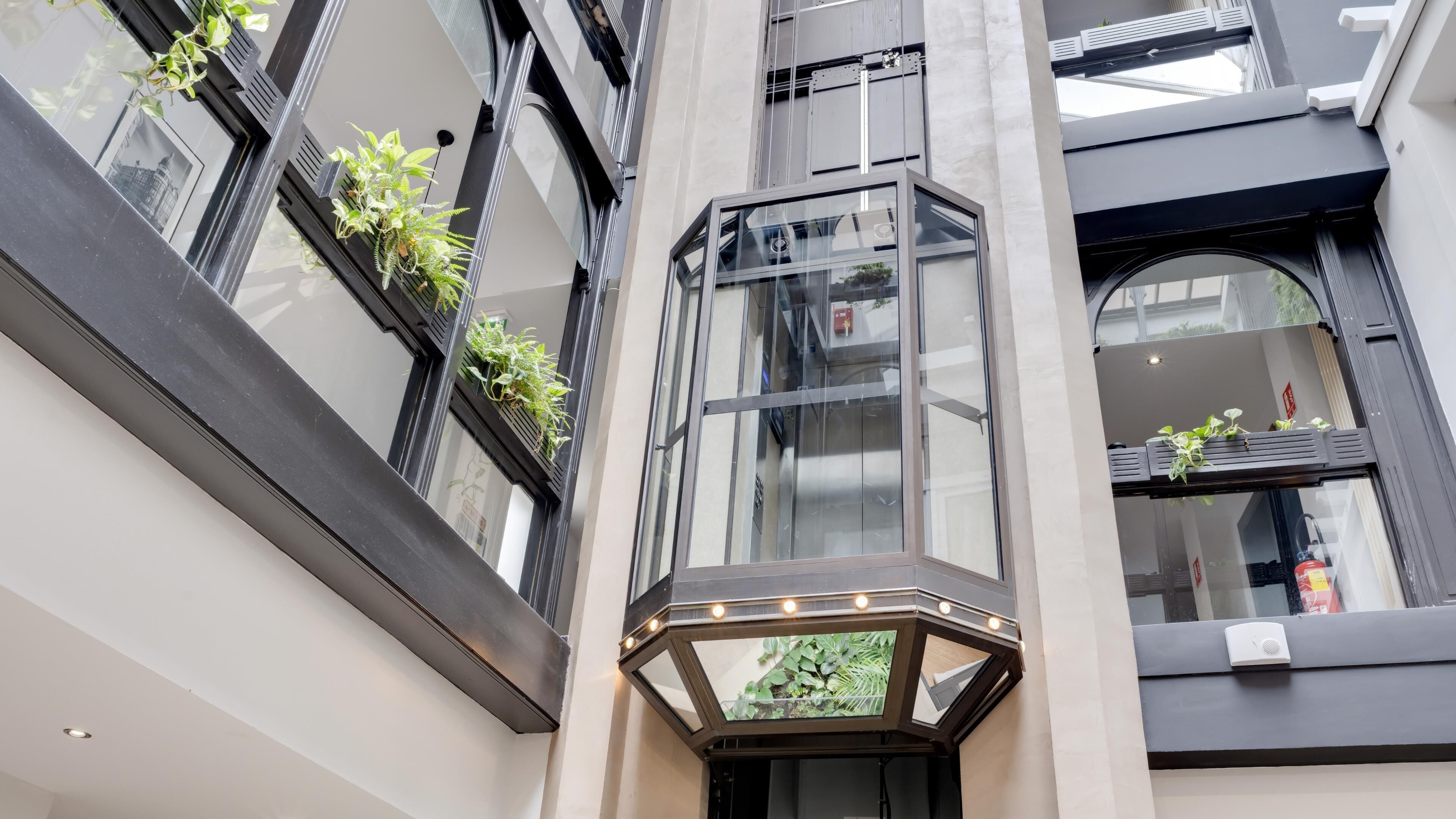 Un edificio moderno con grandes ventanales, una lámpara en esquina y plantas en macetas en los alféizares.