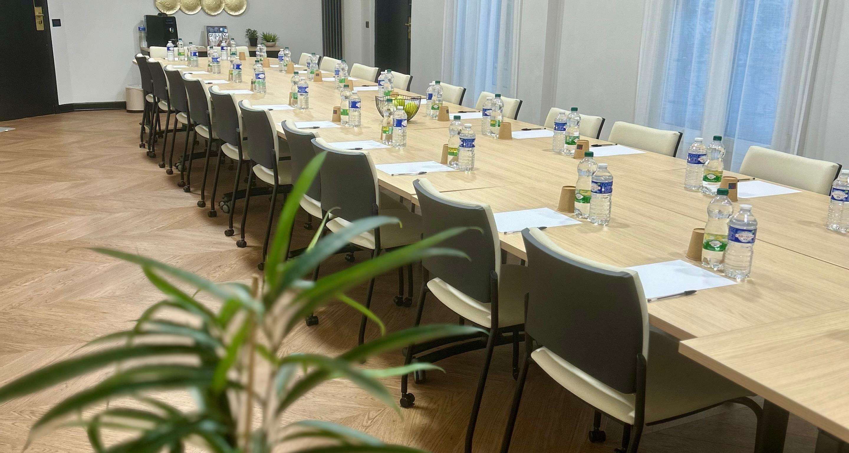 A conference room with a long table, chairs, water bottles, and papers.