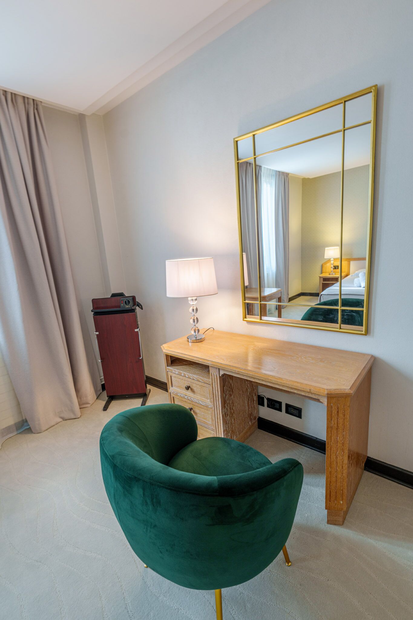 Ein Hotelzimmer mit einem Holztisch, einem grünen Stuhl, einem Spiegel, einer Lampe und einem Kleiderschrank.
