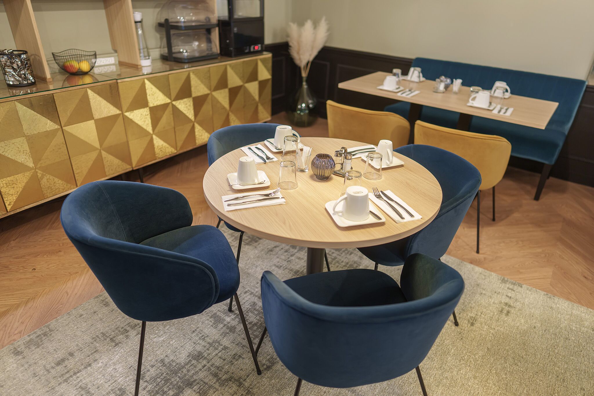 A dining area with a round table set for four, blue chairs, and a geometric-patterned cabinet.