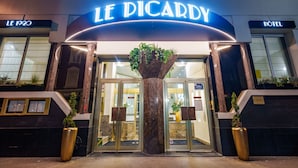 De ingang van Hotel Le Picard, met een marmeren kolom, glazen deuren en potplanten.