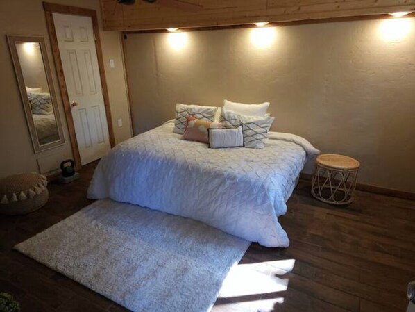 A bedroom with a bed, a bedside table, a small round table, and a mirror. - CHIC COUNTRY HOME IN THE WOODS WITH HOT TUB (Ruidoso)