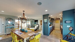 A dining area with a wooden table and yellow chairs, a chandelier, and a view into the kitchen. - Ocean Shore by Distinctive Beach Rentals (Flagler Beach)