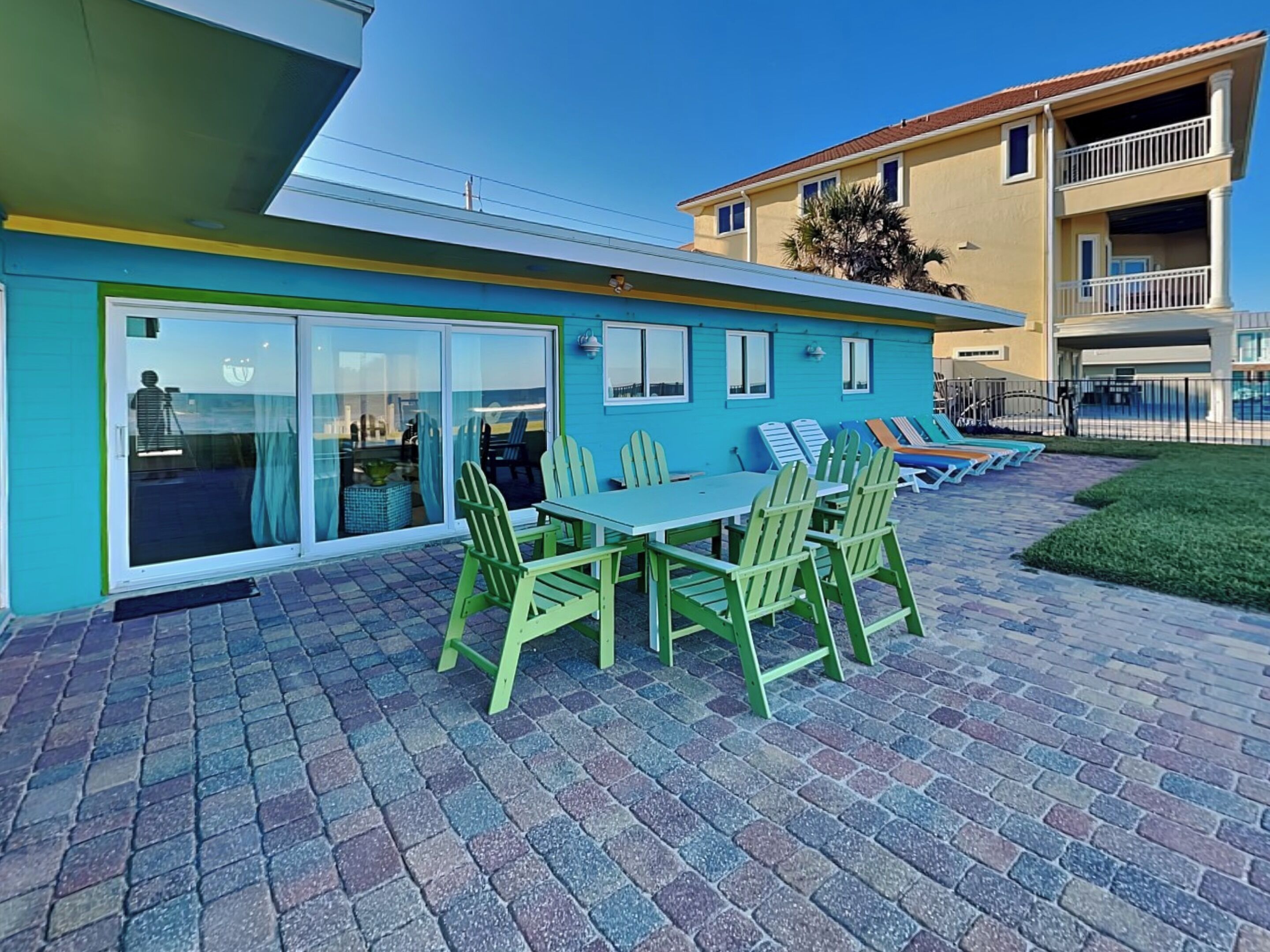 A modern building with a patio area featuring a table and chairs, a glass door entrance, and a view of a neighboring building.
