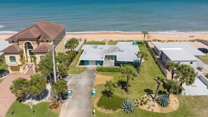 A coastal residential area with a beachfront view, featuring a large house with a tiled roof, a smaller building with a flat roof, and a well-maintained lawn with palm trees. - Ocean Shore by Distinctive Beach Rentals (Flagler Beach)