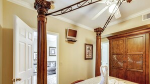 Un dormitorio con una cama, un armario de madera, un ventilador de techo y una puerta que da a otra habitación.