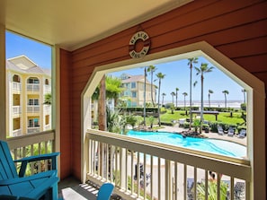 Un balcón con vista a una piscina, palmeras y una playa.