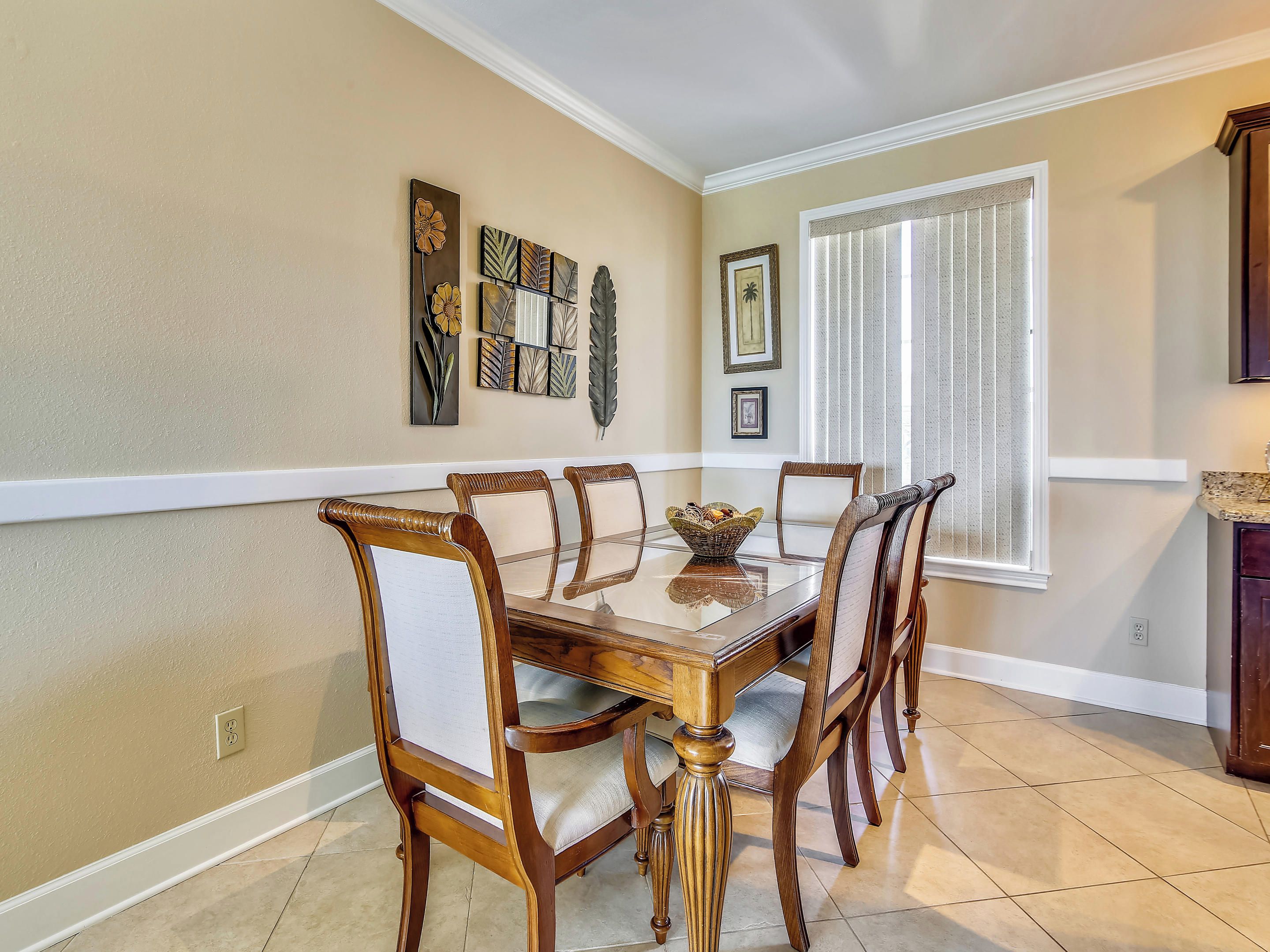 Un comedor con mesa y sillas de madera, una pared decorativa con obras de arte enmarcadas, y una ventana con persianas.