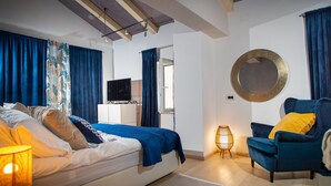 Ein modernes Schlafzimmer mit einem Bett, einem blauen Sessel, einem runden Spiegel und einem Nachttisch mit einer Lampe.