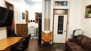 A compact living space with a wooden dining table, a brown leather couch, a TV, and a kitchenette in the background. - Studio in the Heart of East Austin (Austin)