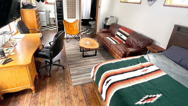 A compact hotel room with a wooden desk, a leather sofa, a bed with a striped blanket, and a small dining table. - Studio in the Heart of East Austin (Austin)