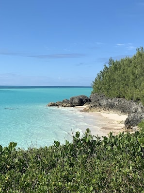 A beach with clear turquoise water, rocky outcrops, and dense green vegetation.