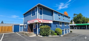 Een gebouw met twee verdiepingen, een 'WELCOME OFFICE' bord, een garage en een motel in de achtergrond.